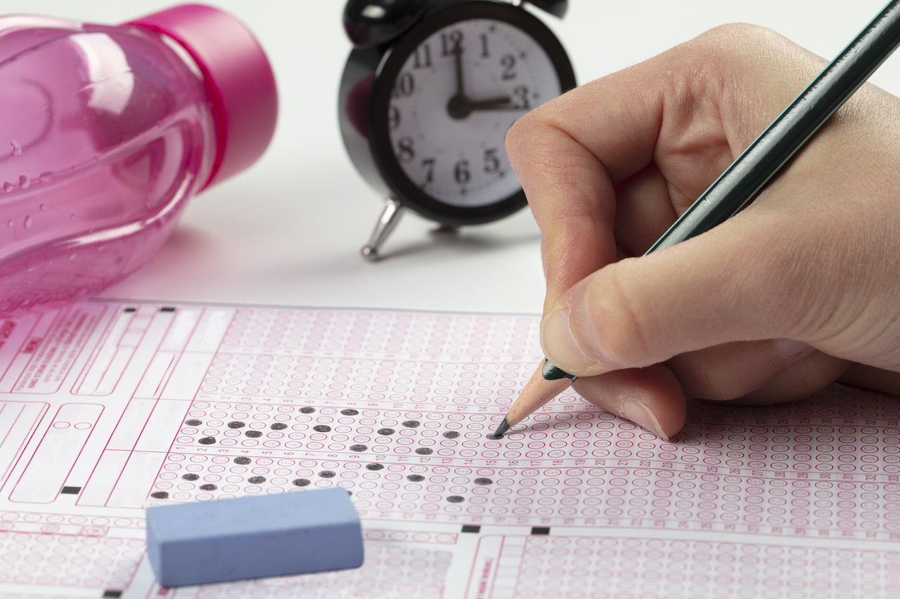 student filling out answer sheet when taking practice test, with a clock in the background