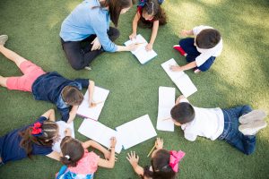 Top view of a group of students and their teacher lying on the grass and learning outdoors