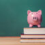 Pink Piggy bank on top of books with chalkboard in the background.