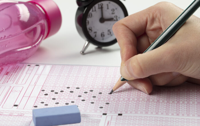 student filling out answer sheet for an exam, with a clock in the background