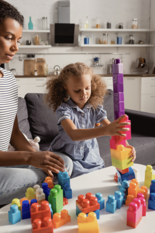 child building tower out of blocks with her mother watching