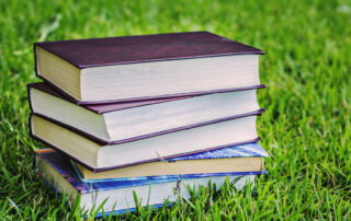 stack of books for summer reading in the grass