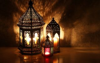Ornamental Arabic lanterns with burning candles on table glowing at night, festive greeting card, invitation for Muslim holy month Ramadan Kareem. Iftar dinner background with golden glow.
