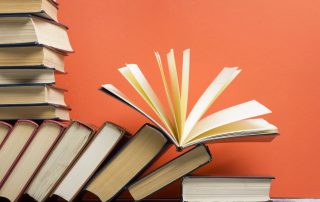 Books by AAPI authors, stacks of books in front of bright orange background.