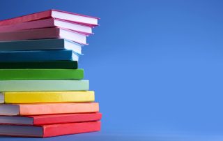Several colorful books stacked to make a rainbow for pride month reading.