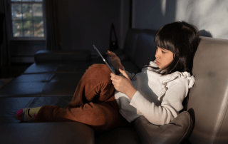 Child using an ipad on a large couch, dark background.