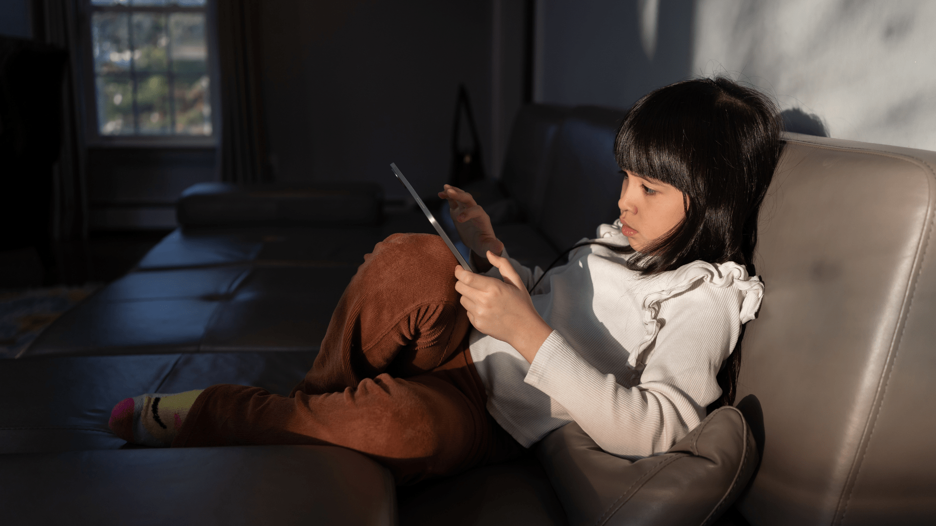 Child using an ipad on a large couch, dark background.